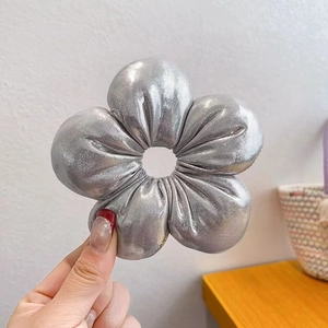 Detailansicht eines silbernen Blumen-Haargummis mit metallisch glänzender Textur