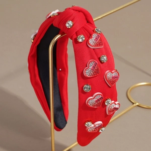 Détail d'un bandeau noué rouge avec strass, breloques en cœur et texte LOVE sur support doré