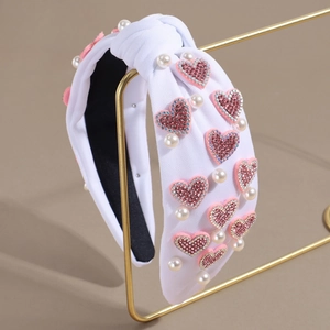 Détail d'un serre-tête noué blanc avec cœurs en strass roses et perles sur support doré