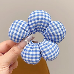 Detail eines blau-weiß karierten Stoff-Haargummis in Blumenform auf grauem Grund