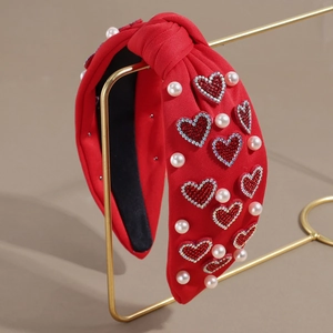 Détail d'un serre-tête rouge noué avec des cœurs en strass et perles sur support