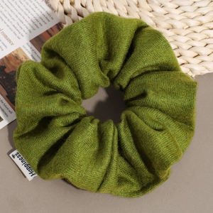 Detailed macro view of a green knitted scrunchie with a Happiness label on textured background