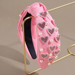 Détail d'un serre-tête rose noué avec des paillettes cœur et des perles sur un support