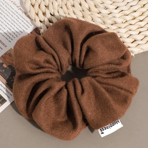 Detail of dark brown knitted scrunchie texture with a white Happiness woven label