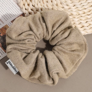 Detailed view of khaki knitted scrunchie texture with a white Happiness label tag