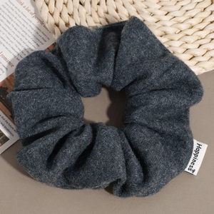 Close-up of a dark grey wool scrunchie with Happiness label on a rustic magazine background