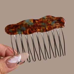 Detailed macro view of 10-tooth metal hair comb with amber acetate wave pattern
