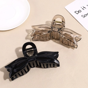 Large 3D bow hair claw clips in glossy black and amber shown on a minimalist table