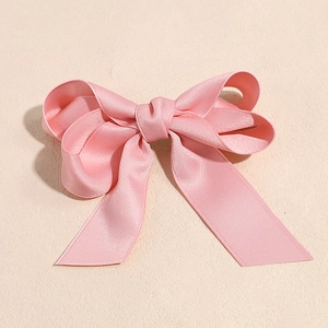 Detail of pink satin bow hair clip with long ribbons and smooth glossy texture
