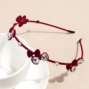 Détail d'un serre-tête en velours rouge avec strass, breloques cœurs et perles blanches