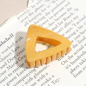 Close-up of ginger yellow triangular hair claw with silver glitter on magazine background