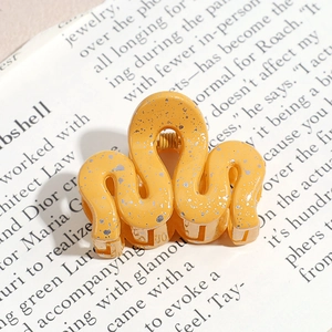 Minimalist yellow wavy hair claw clip with ink splash pattern on a magazine background