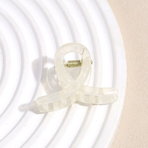 Vue détaillée d'une mini pince à cheveux blanc crème avec un ressort en métal doré