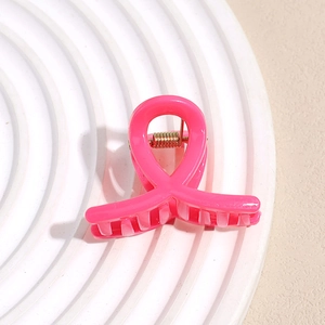 Gros plan d'une pince à cheveux rose brillant en forme de ruban sur un plateau blanc
