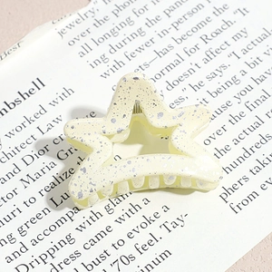 Detail of star-shaped hair claw clip in cream yellow with silver splatter texture