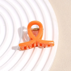 Détail d'une pince à cheveux orange vif en forme de ruban avec un ressort métallique doré