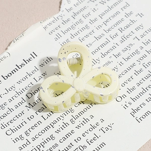 Macro detail of cream resin hair claw with silver splash pattern on vintage newspaper