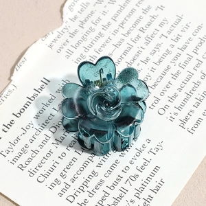 Detailed close-up of a translucent dark teal flower-shaped hair claw clip with glossy resin