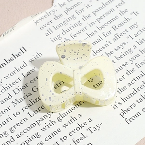 Macro shot of cream bow hair claw clip with silver ink splatter and metal spring