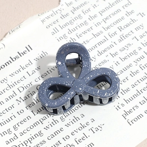 Detail of grey ink-splatter resin hair claw clip resting on vintage newspaper background