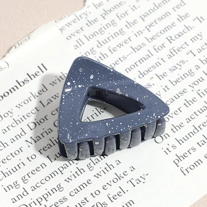 Detail of dark blue triangular hair claw clip with silver ink splatter texture on paper