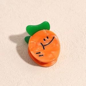 Détail de pince à cheveux carotte avec visage souriant et feuilles vertes sur fond beige