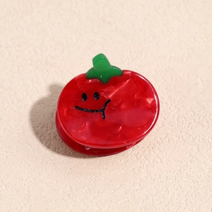 Détail de la pince à cheveux tomate rouge avec texture marbrée et motif visage souriant