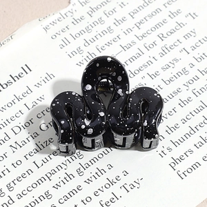 Macro detail of wave-shaped black hair claw clip with silver speckles on vintage book