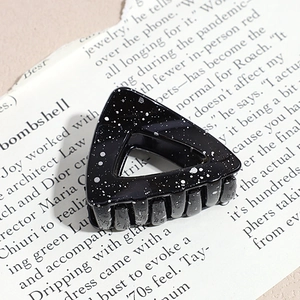 Macro view of black triangular hair claw with white ink splatter on newspaper background