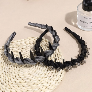Padded headband with rhinestones and black spikes displayed on a round woven mat