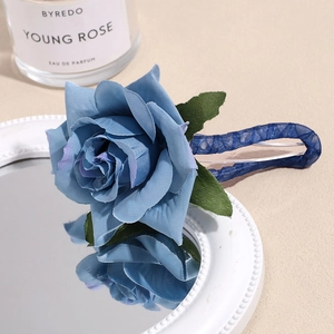 Detail of blue silk rose hair clip with green leaves and mesh handle on white mirror