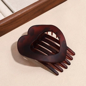 Detail of hollow heart-shaped hair claw in dark amber resin on beige textured background