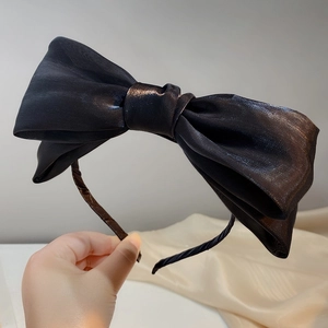Detalle de una diadema con lazo grande de satén negro con textura brillante