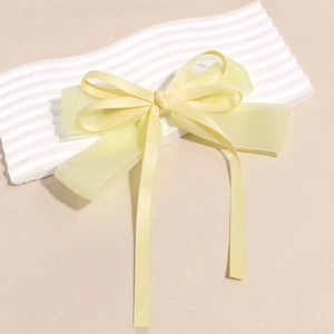Detail of a bright yellow organza bow hair clip with satin ribbons on white display board