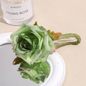 Detailed view of the realistic light green silk rose hair clip on a reflective mirror surface