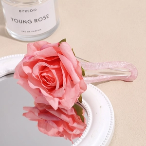 Detail shot of a pink 3D fabric rose hair clip resting on a round mirror edge