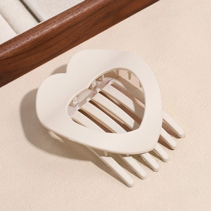 Detail of a beige matte hollow heart hair claw clip on a minimalist textured surface
