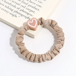 Detailed view of apricot pleated fabric scrunchie with 3D heart accessory on open book