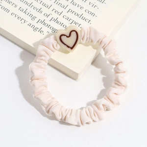 Detailed shot of cream satin scrunchie with 3D heart charm and pleated fabric texture