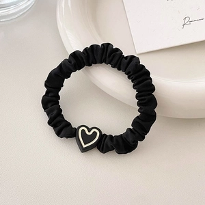 Minimalist black ruffled hair scrunchie with a contrast heart charm on a ceramic plate