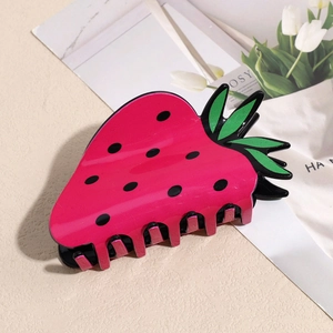 Dettaglio della molletta per capelli a fragola rosa con foglia verde e semi neri su carta