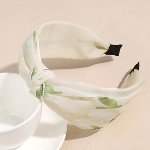 Primer plano de la diadema de nudo floral en tela crema con estampado de hojas en taza