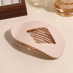 Détail d'une pince à cheveux ovale beige mat avec une découpe élégante en losange
