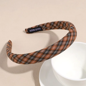 Close-up of brown plaid fabric headband with handmade label on beige background