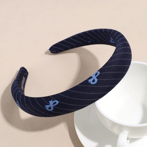 Detail of navy twill headband with bow embroidery and handmade tag by coffee cup