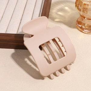 Detail of a large beige matte square hair claw clip on an elegant wooden jewelry tray