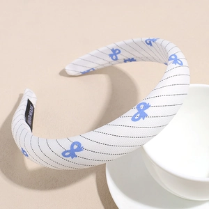 Detail showing white fabric hair hoop with navy patterns and woven handmade label
