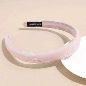 Detail of pink satin headband with floral patterns and a woven Handmade label inside