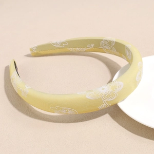 Detail of yellow satin headband featuring white floral patterns and padded fabric design