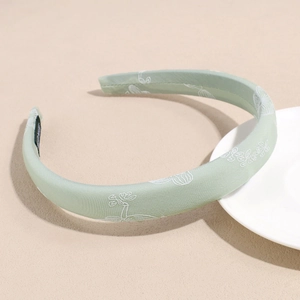 Detail of mint green floral satin headband with elegant white embroidered flower patterns